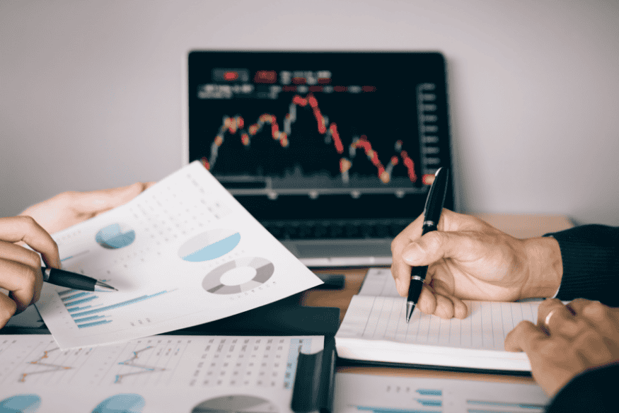 Zwei Personen besprechen Anleihe-Portfolio und Kennzahlen vor einem Bildschirm mit fallenden Kursen