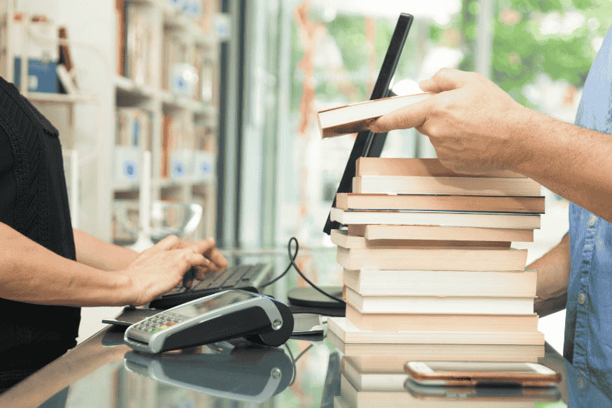 Vater kauft einen Stapel Schulbücher – typische laufende Kosten für Kinder im Familienbudget.