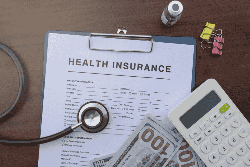Formular zur Krankenversicherung mit Stethoskop, Geldscheinen und Taschenrechner auf einem Schreibtisch.