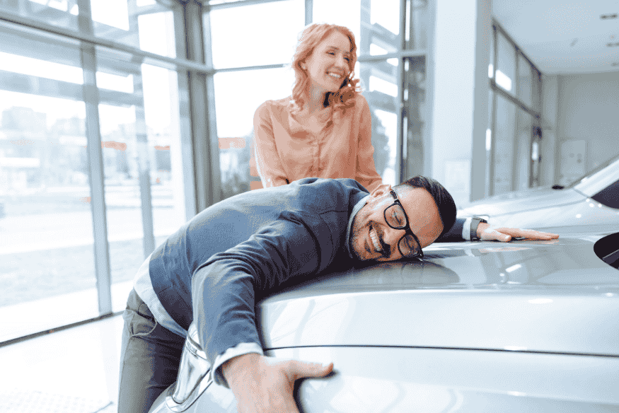 Paar freut sich im Autohaus über neues Auto und zeigt, wie sich große Anschaffungen mit gut gesetzten Sparzielen erfüllen lassen.