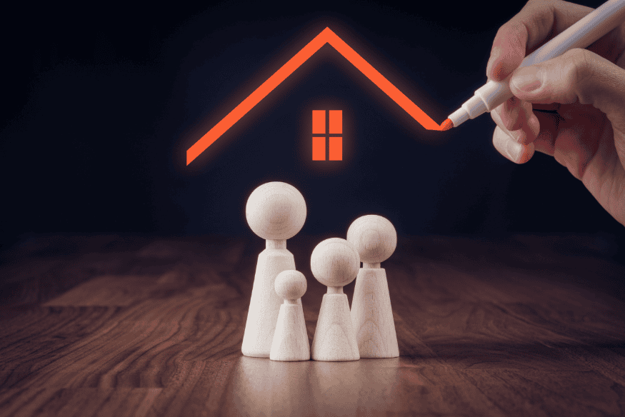 Holzfiguren einer Familie unter einem gezeichneten Hausdach – Darstellung des Schutzes durch eine Hausratversicherung.