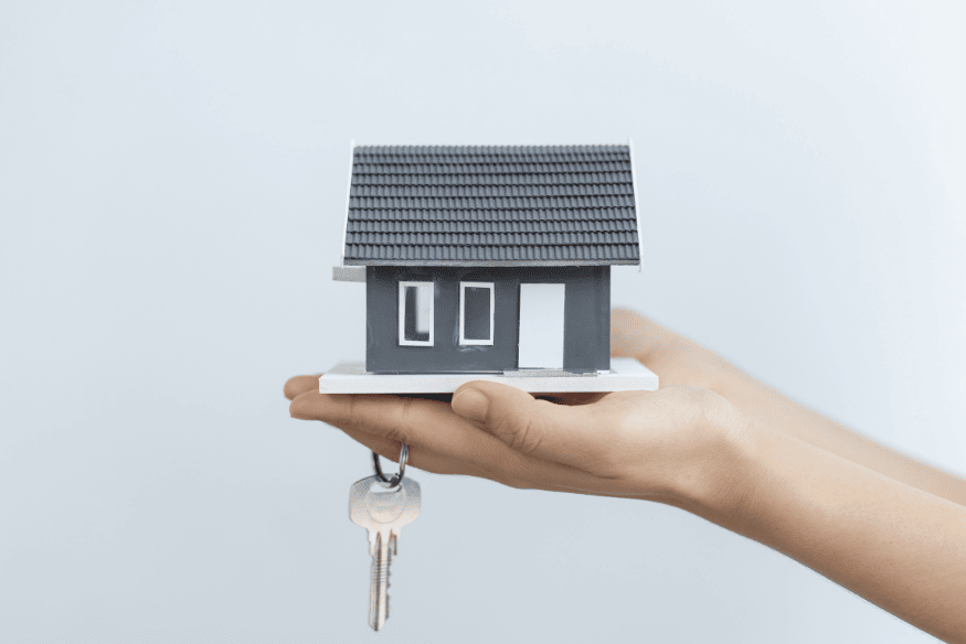 Kleine Modellhaus in einer Hand mit Schlüsselbund – Symbol für Schutz und Absicherung durch eine Hausratversicherung.