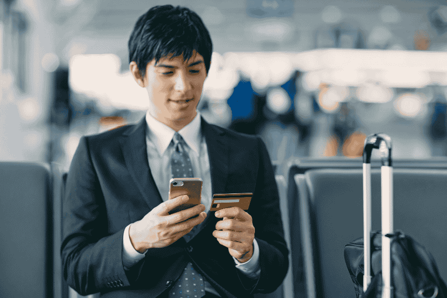 Geschäftsreisender nutzt Smartphone und Kreditkarte im Flughafen – Hinweis auf Meilensammeln durch Reisen und Ausgaben.