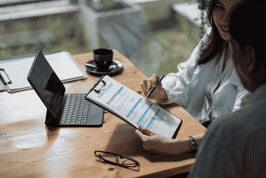 Beratungsgespräch über private Pflegezusatzversicherung mit Formular und Tablet am Tisch.