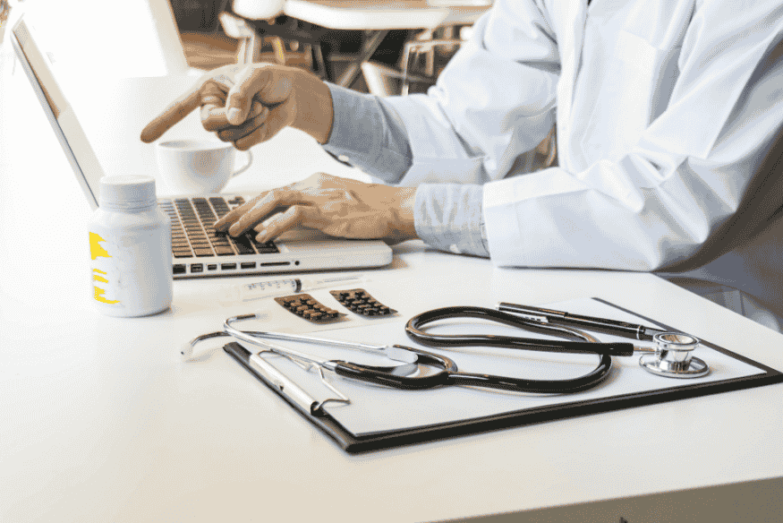 Arzt arbeitet am Laptop und überprüft medizinische Unterlagen als Vorbereitung für eine Reise-Krankenversicherung.