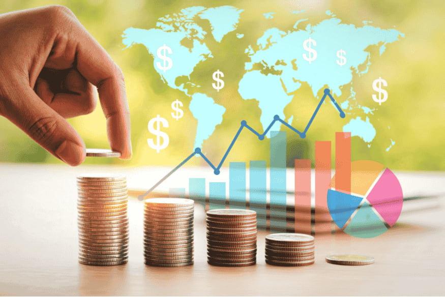 Hand stapelt Münzen vor Weltkarte und Diagrammen zu Kapitalerträgen