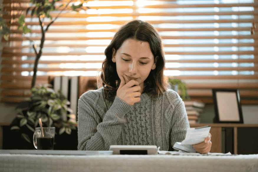 Frau zu Hause mit Taschenrechner und Belegen bei der Prüfung variabler Kosten im Haushaltsplan und der Kontrolle monatlicher Ausgaben